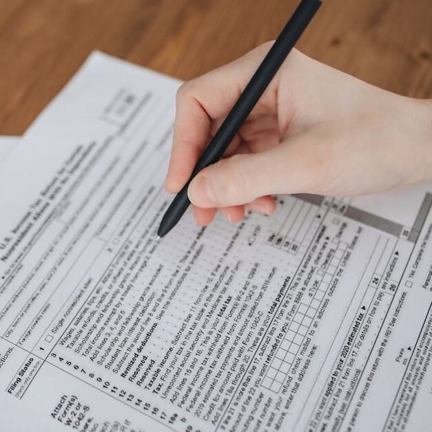 Close-up of a hand writing on tax documents with a black pen.