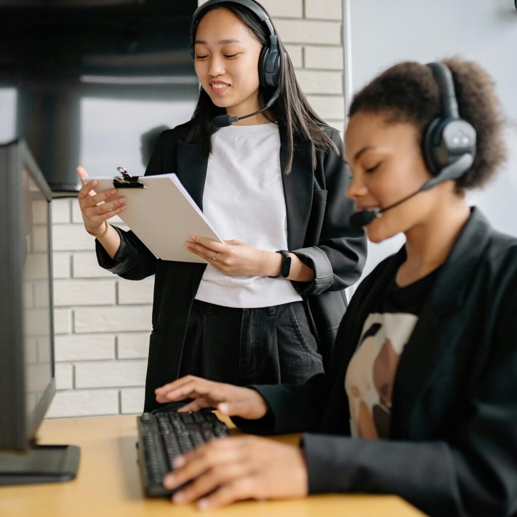 Two women in a call center working with headsets and computers, focusing on customer support.
